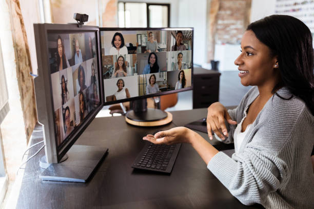 The attractive mid adult woman teleconferences to meet with her diverse colleagues.  She is social distancing due to the coronavirus epidemic.